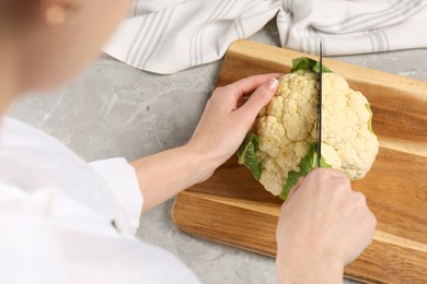 Woman cutting fresh cauliflower at light grey table, closeup