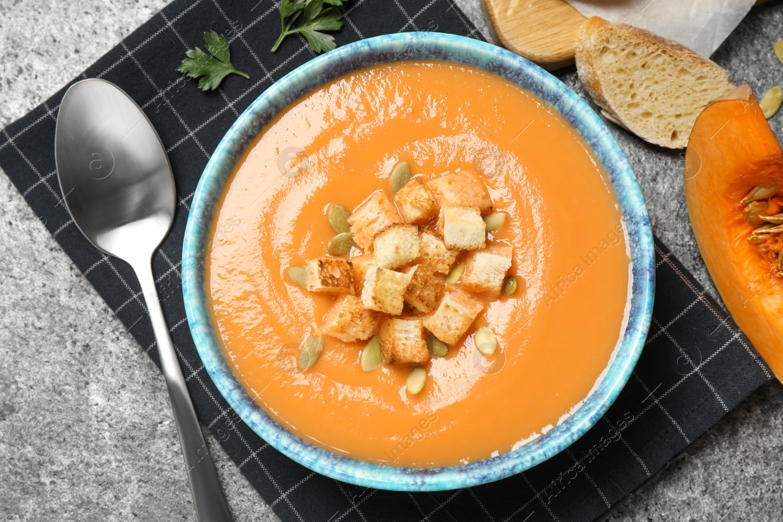 Photo of Tasty creamy pumpkin soup with croutons and seeds in bowl on grey table, flat lay