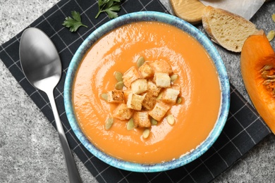 Photo of Tasty creamy pumpkin soup with croutons and seeds in bowl on grey table, flat lay