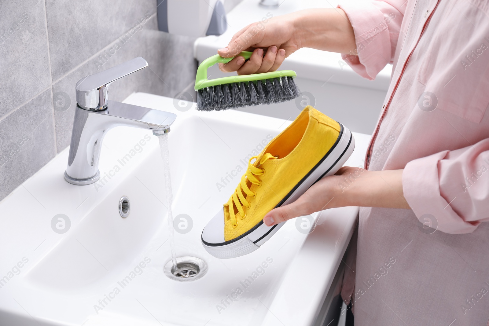 Photo of Woman washing stylish sneakers with brush in sink, closeup