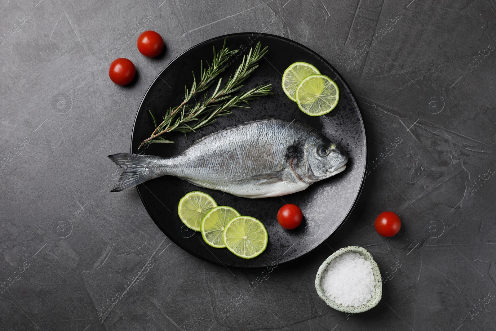Photo of Fresh dorado fish, lime, tomatoes and rosemary on grey table, top view