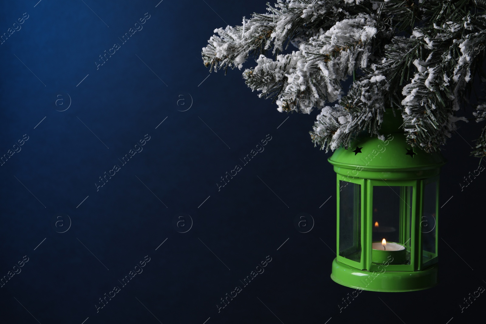 Photo of Christmas lantern with burning candle on fir tree against blue background, closeup. Space for text