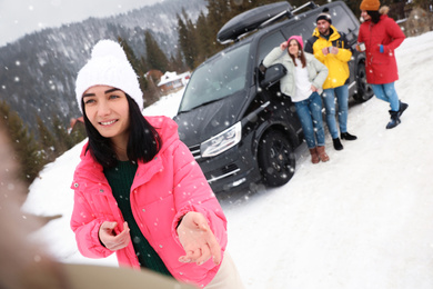 Photo of Group of friends near car on snowy road. Winter vacation