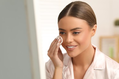 Photo of Beautiful woman removing makeup with cotton pad indoors, space for text