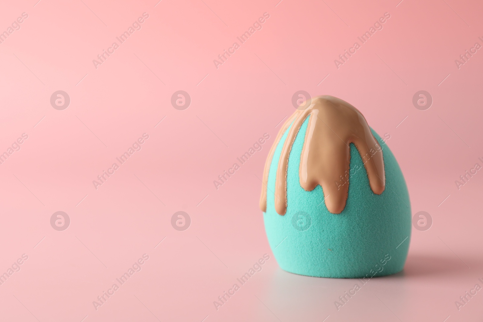 Photo of Makeup sponge with skin foundation on pink background, space for text