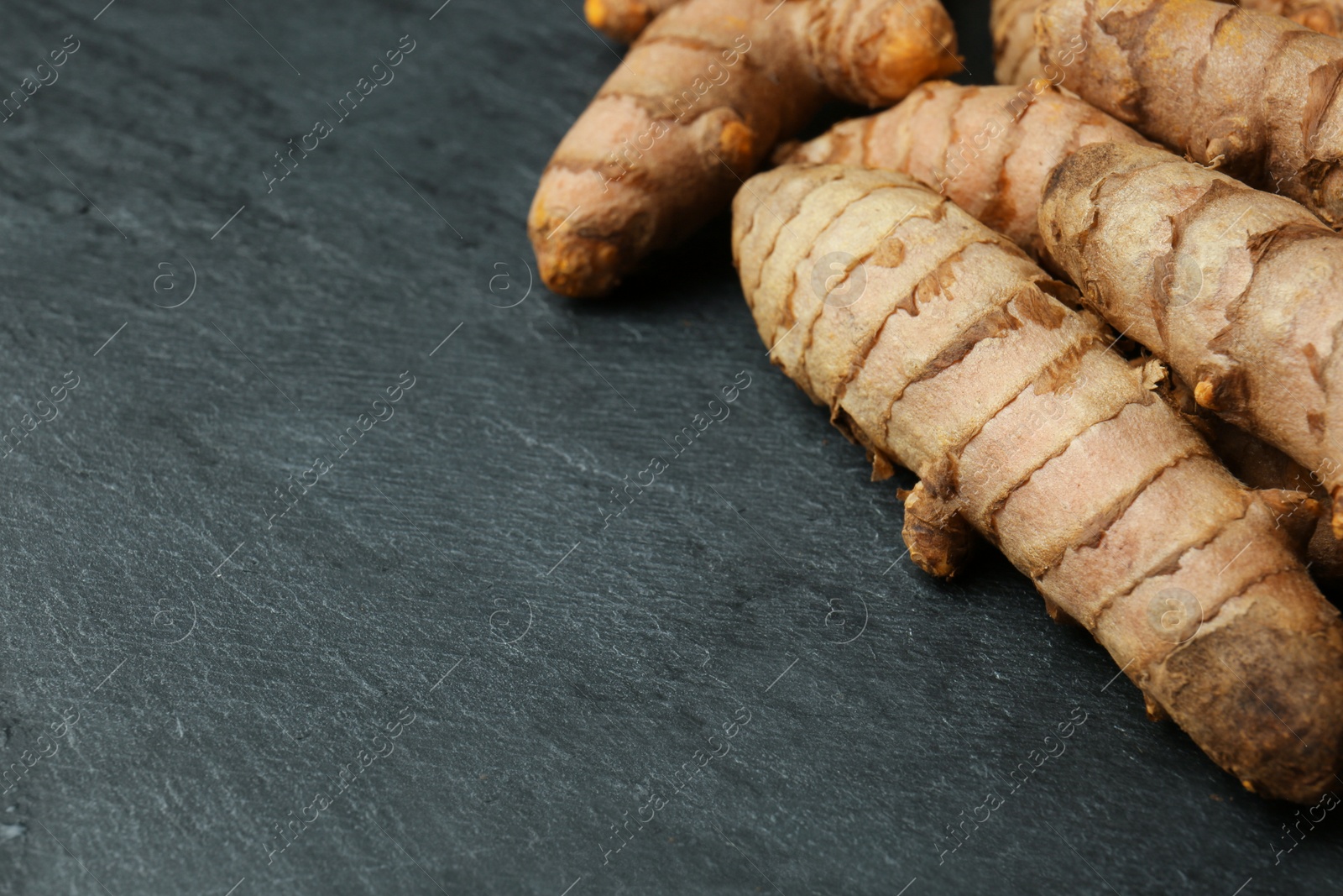 Photo of Many raw turmeric roots on black textured table, closeup. Space for text