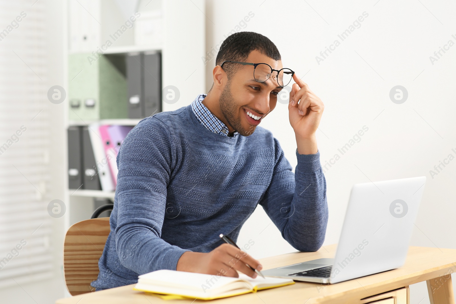 Photo of Smiling African American man writing in notebook at wooden table