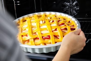 Photo of Woman putting raw traditional English apple pie into oven, closeup