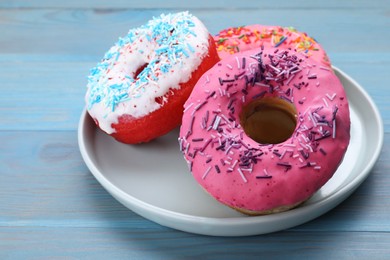 Photo of Sweet glazed donuts decorated with sprinkles on light blue wooden table, closeup. Tasty confectionery