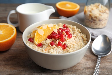 Photo of Bowl of quinoa porridge with nuts, orange and pomegranate seeds served for breakfast on wooden table