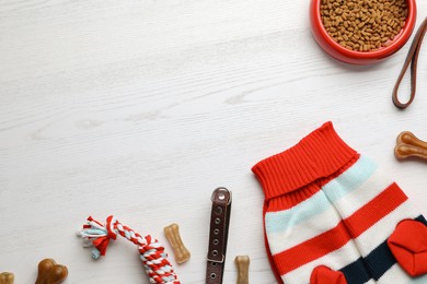 Flat lay composition with dog clothes, food and accessories on white wooden table. Space for text