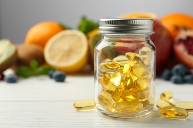 Vitamin pills in bottle and fresh fruits on white wooden table, closeup. Space for text