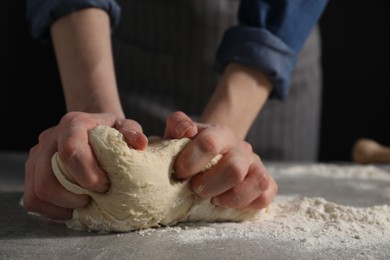 Photo of Making bread. Woman kneading dough at table on dark background, closeup. Space for text