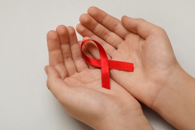 Photo of Little girl holding red ribbon on beige background, closeup. AIDS disease awareness