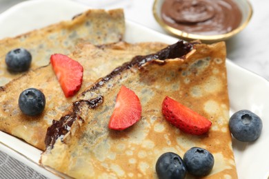Photo of Tasty crepes with chocolate paste and berries served on table, closeup