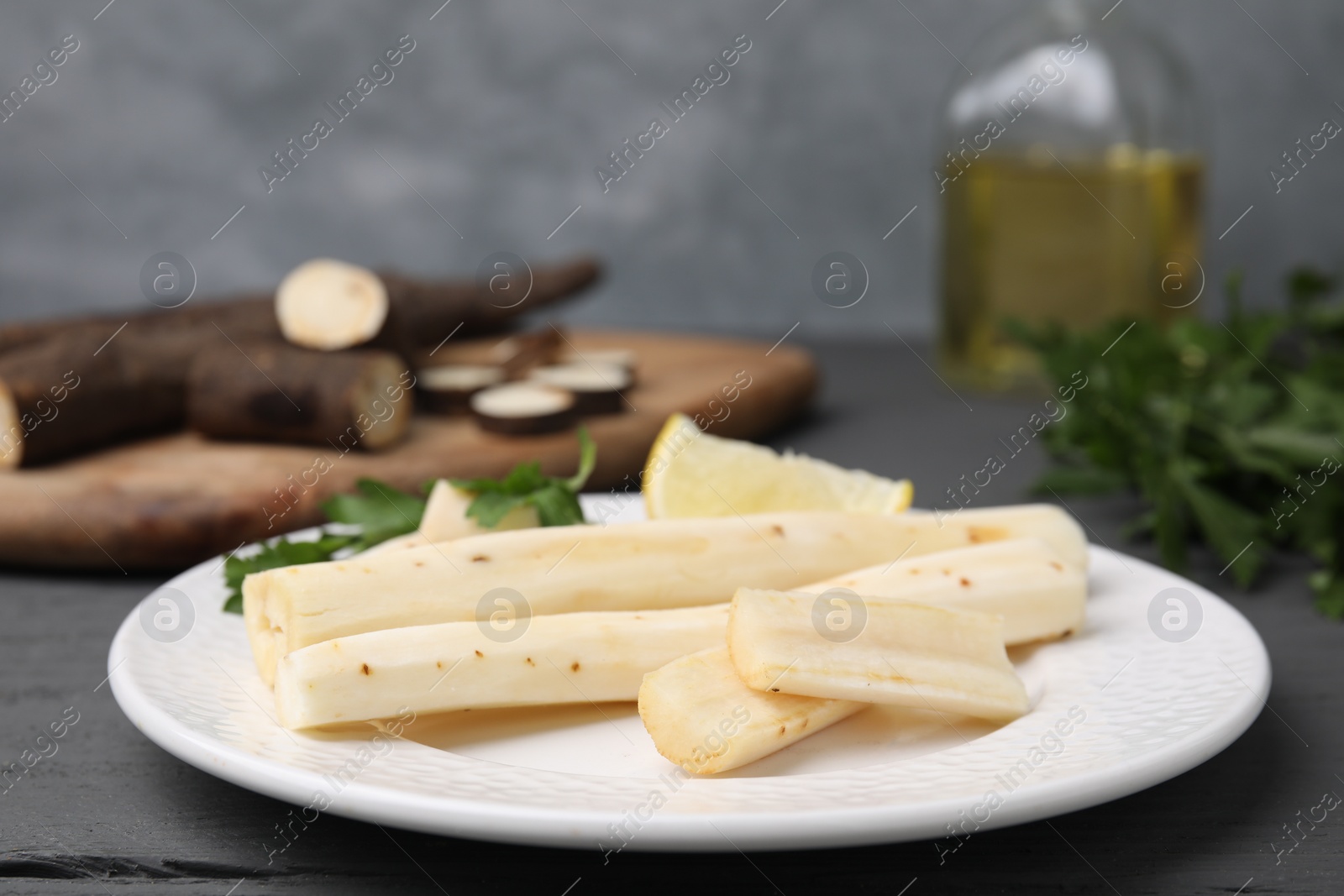 Photo of Cut raw salsify roots with parsley and lemon on grey wooden table, closeup