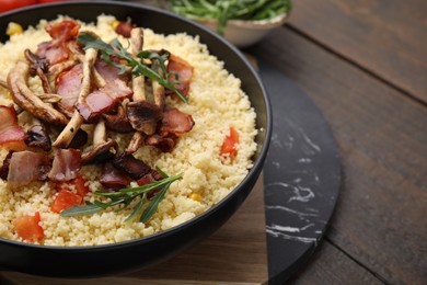 Photo of Tasty couscous with mushrooms and bacon in bowl on wooden table, closeup. Space for text