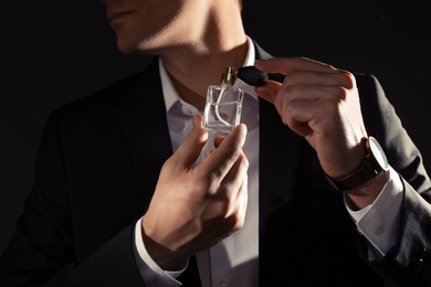 Handsome man applying perfume on neck against black background, closeup