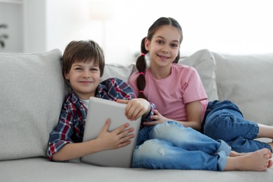 Happy brother and sister with tablet on sofa at home