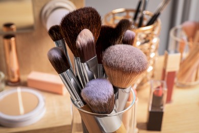 Set of professional brushes and makeup products near mirror on wooden table, closeup