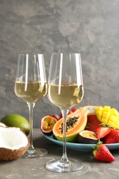 Delicious exotic fruits and glasses of wine on grey table