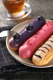 Photo of Different tasty glazed eclairs served on grey textured table, closeup