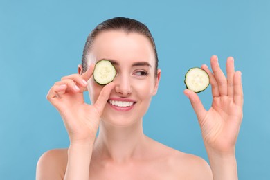 Photo of Beautiful woman covering eye with piece of cucumber on light blue background
