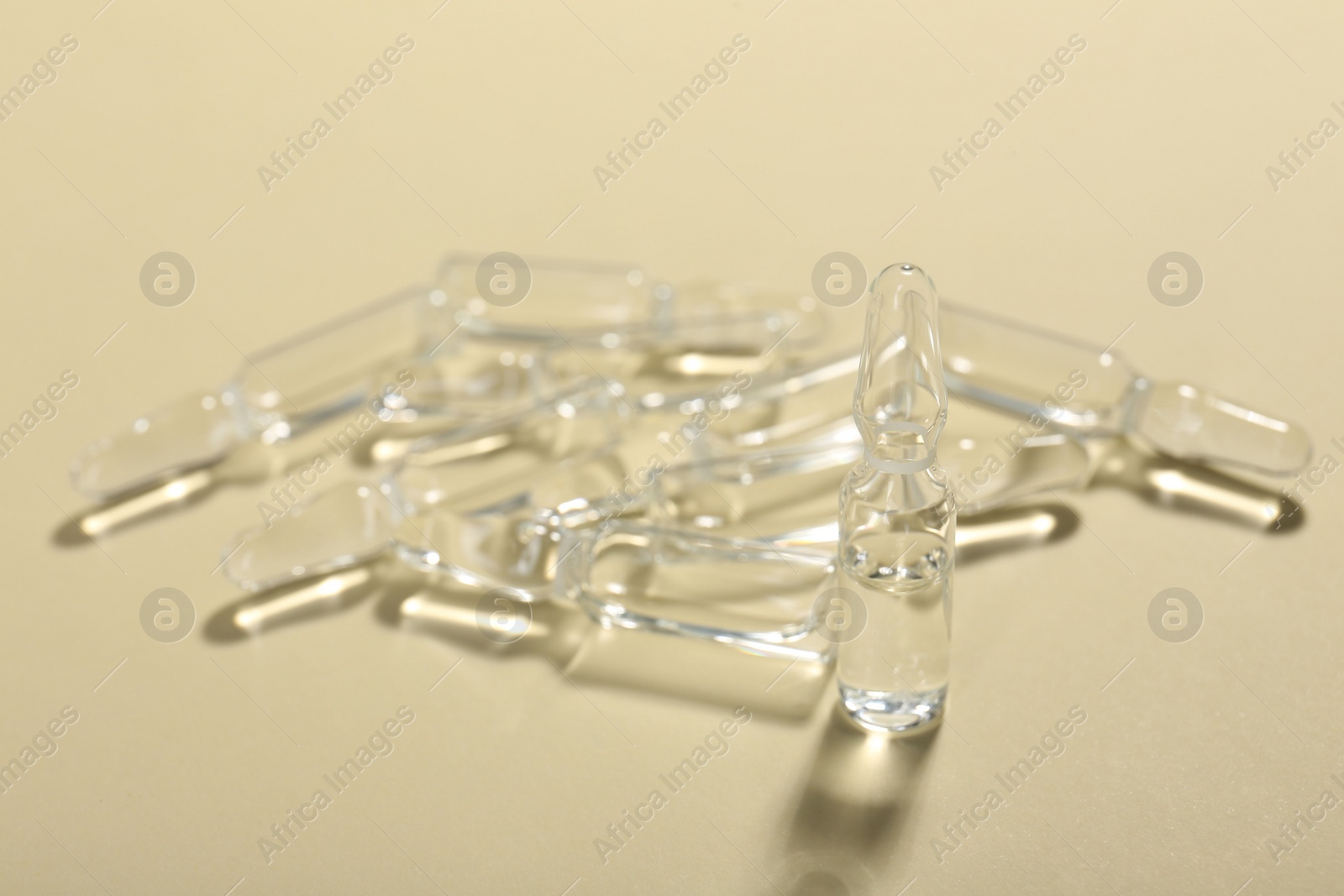 Photo of Glass ampoules with liquid on beige background, closeup