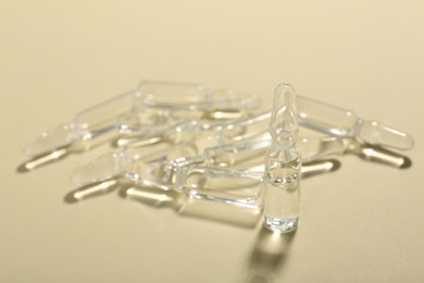 Glass ampoules with liquid on beige background, closeup