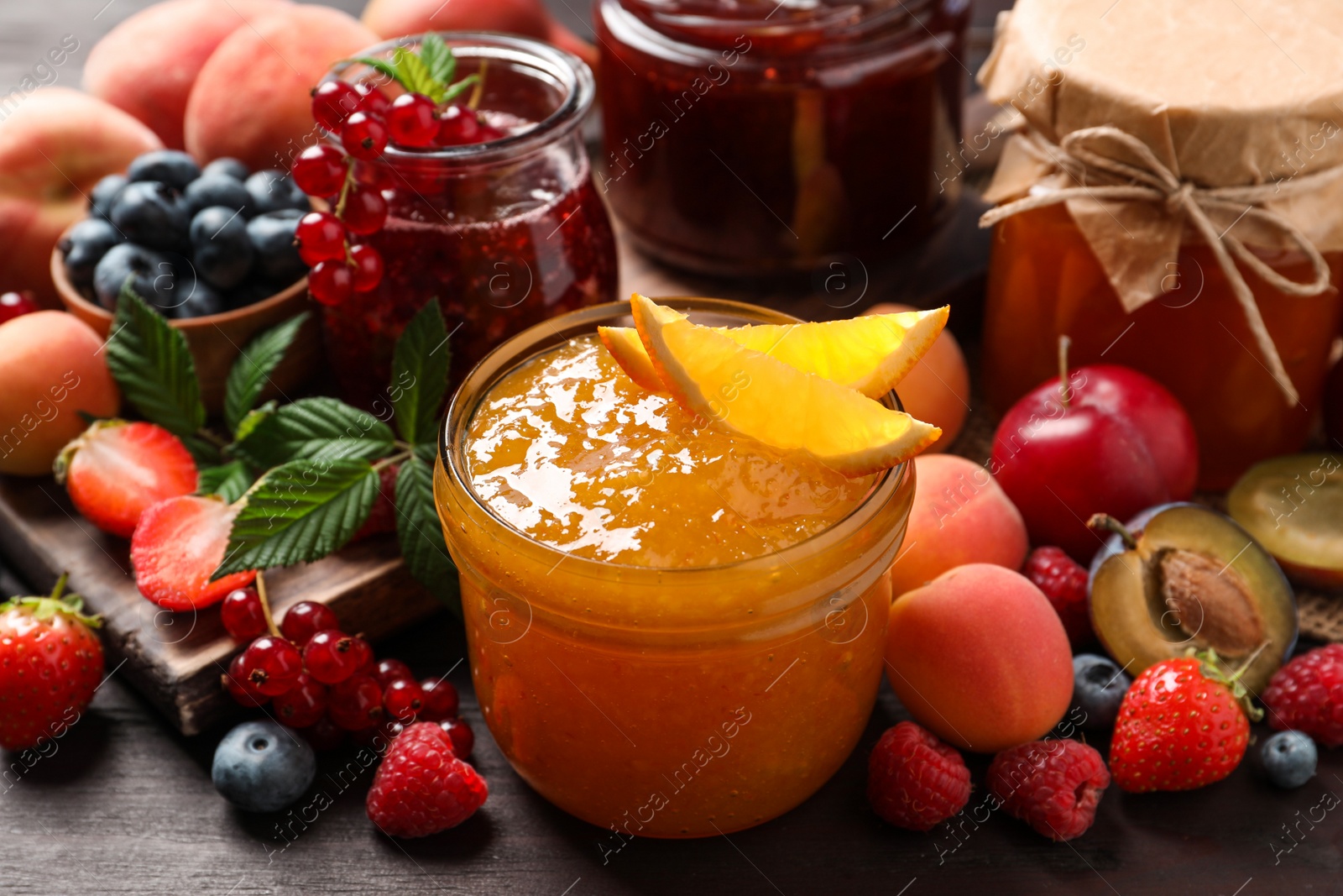 Photo of Jars with different jams and fresh fruits on wooden table, closeup