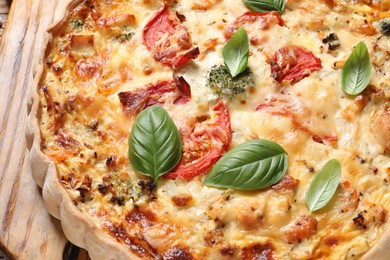 Photo of Tasty quiche with tomatoes, basil and cheese on wooden table, closeup