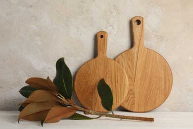 Wooden cutting boards and floral decor on white table near textured wall