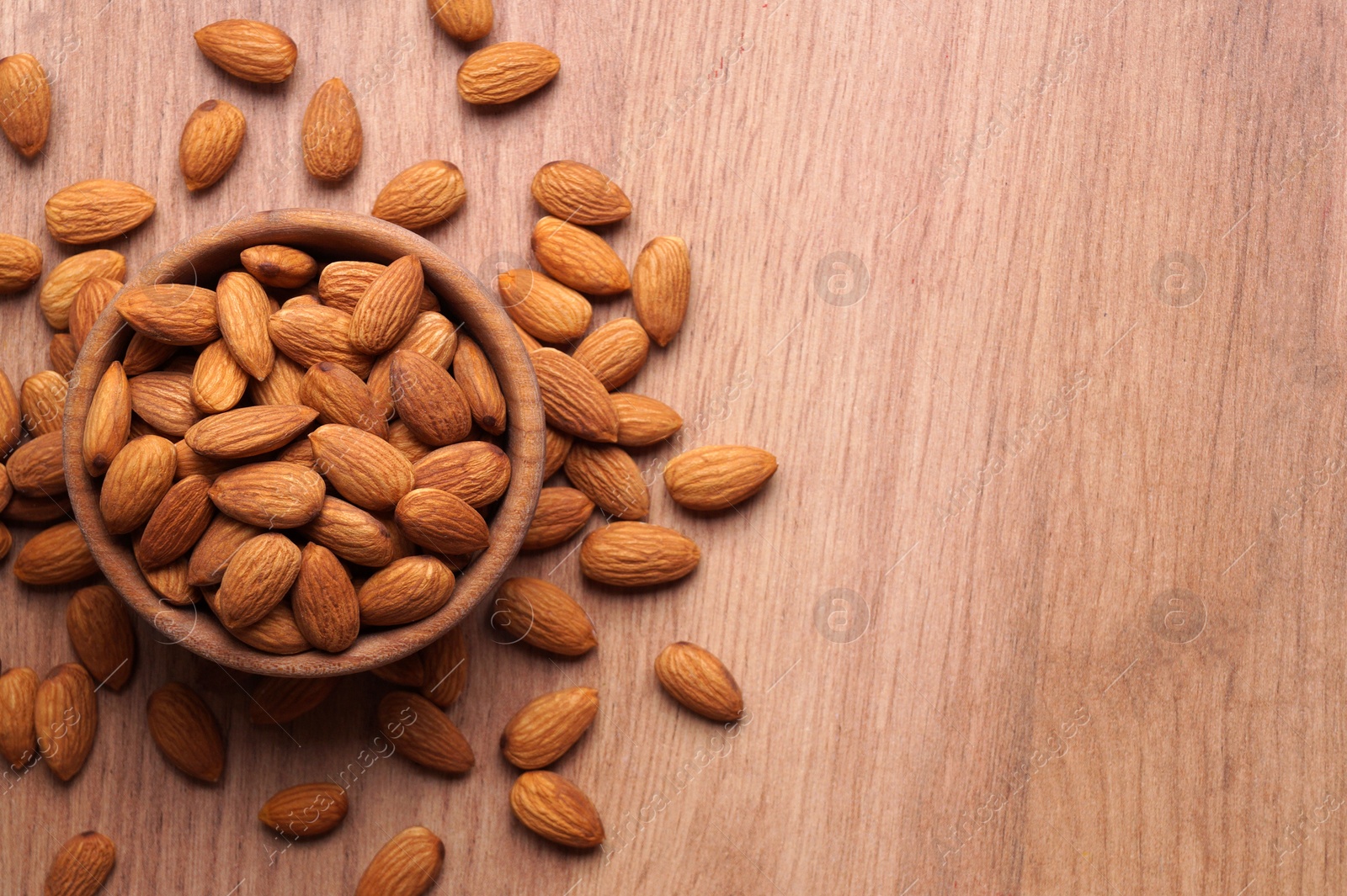 Photo of Tasty almonds in bowl on wooden table, flat lay. Space for text