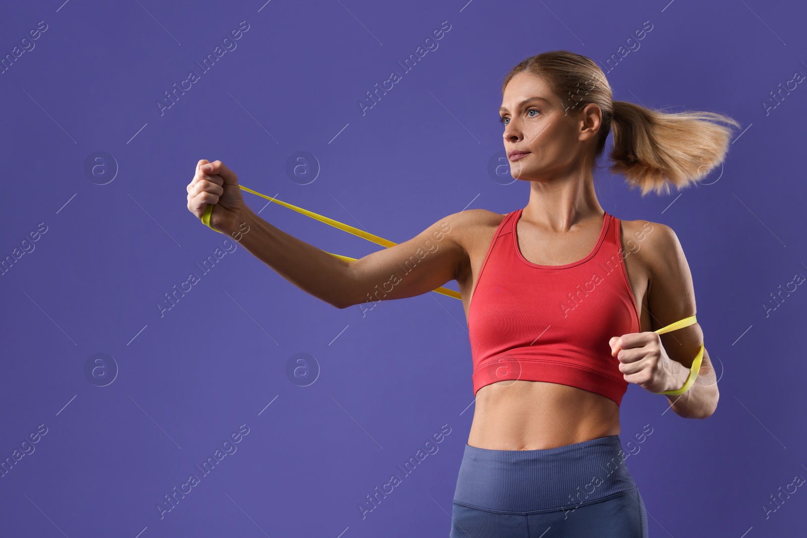 Photo of Athletic woman exercising with elastic resistance band on purple background