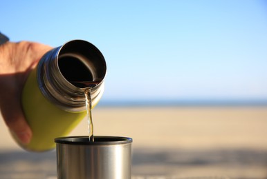 Photo of Woman pouring hot drink from yellow thermos into cap outdoors, closeup. Space for text