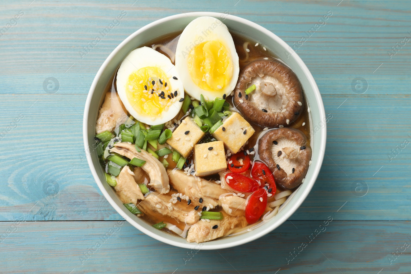 Photo of Bowl of delicious ramen on light blue wooden table, top view. Noodle soup