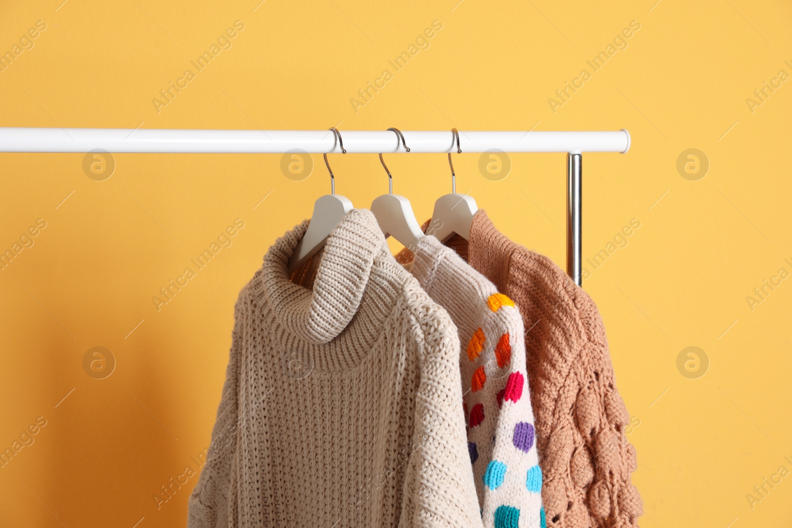 Photo of Collection of warm sweaters hanging on rack against color background