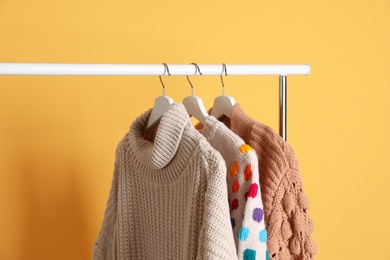 Collection of warm sweaters hanging on rack against color background