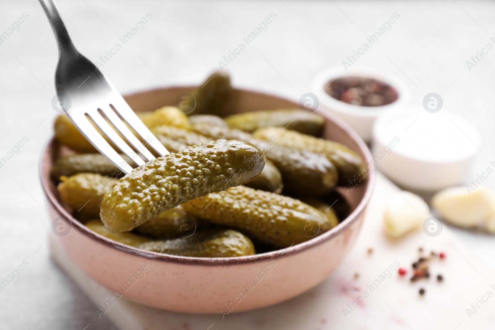 Photo of Fork with pickled cucumber over bowl on light table, closeup