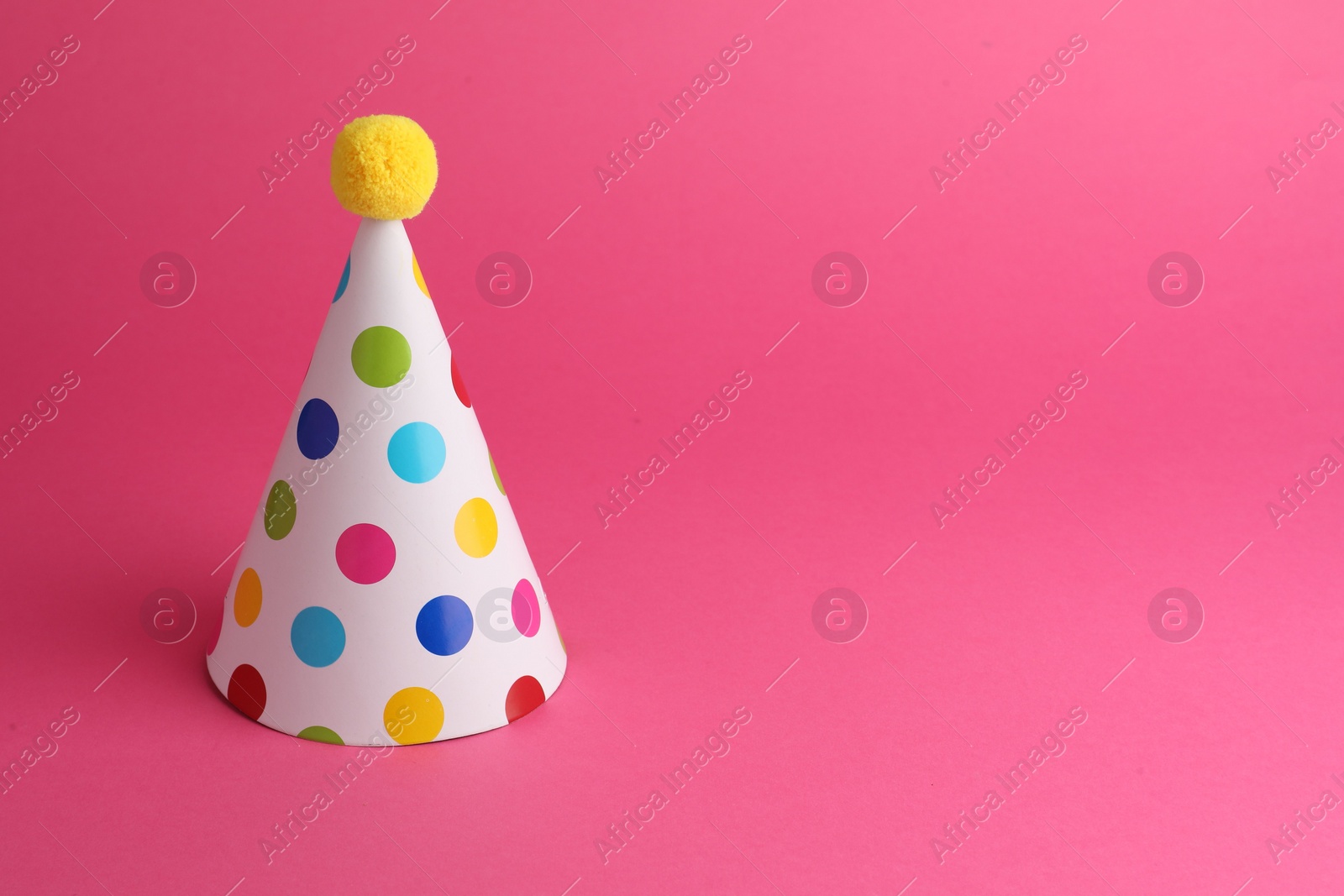 Photo of One beautiful party hat with pompom on pink background, space for text