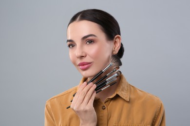 Photo of Beautiful woman with different makeup brushes on light grey background