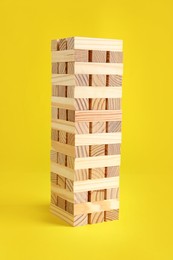 Photo of Jenga tower made of wooden blocks on yellow background