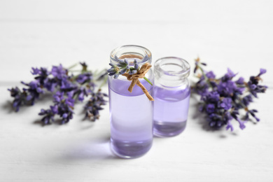 Photo of Bottles of essential oil and lavender flowers on white wooden table