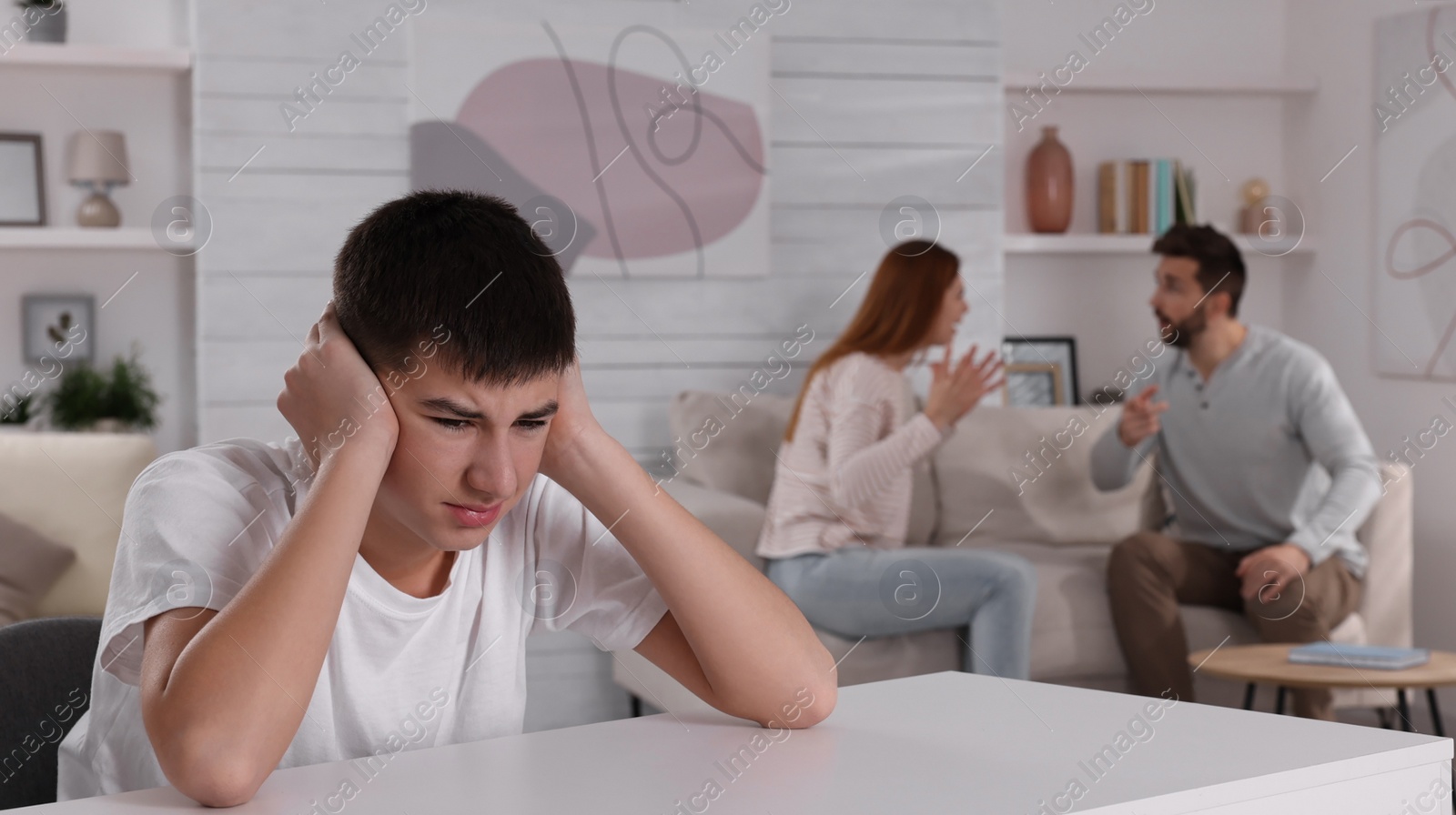 Photo of Unhappy teenage boy covering ears while his parents arguing on background. Problems at home