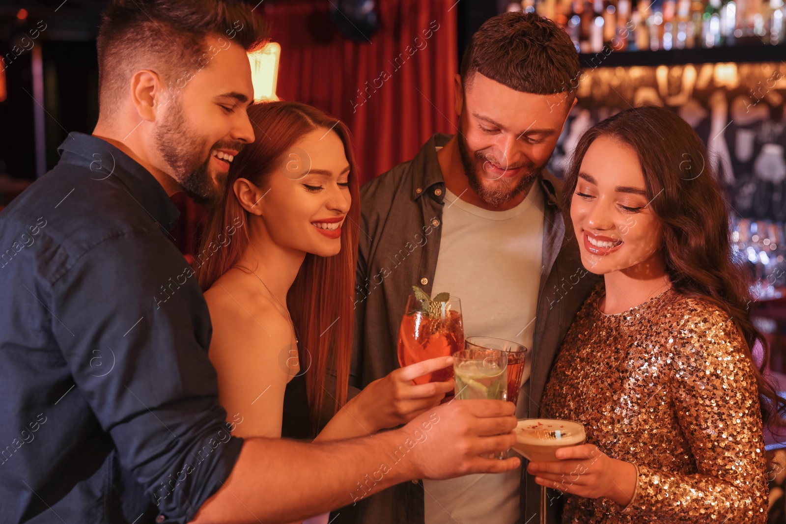 Photo of Happy friends clinking glasses with fresh cocktails in bar