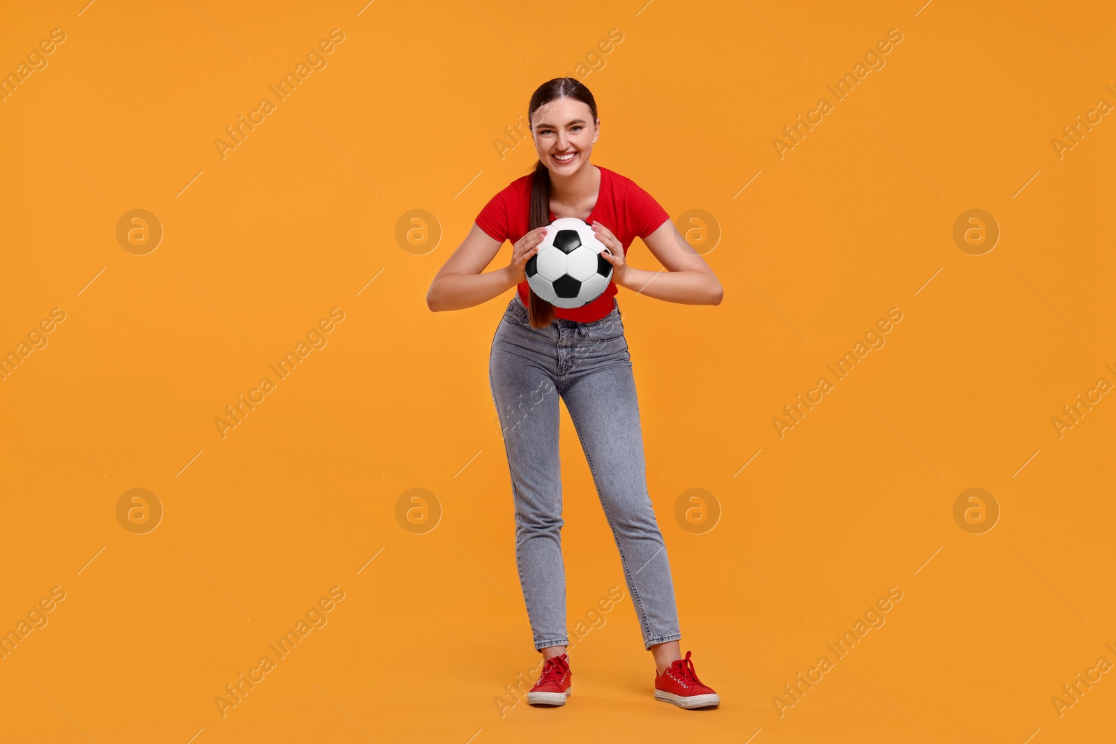 Photo of Happy soccer fan with ball on orange background