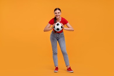 Photo of Happy soccer fan with ball on orange background