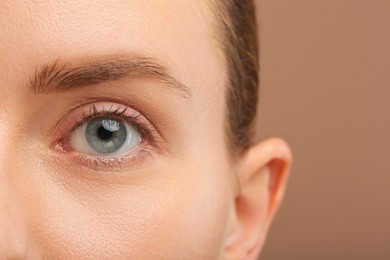 Photo of Woman with beautiful natural eyelashes on light brown background, closeup