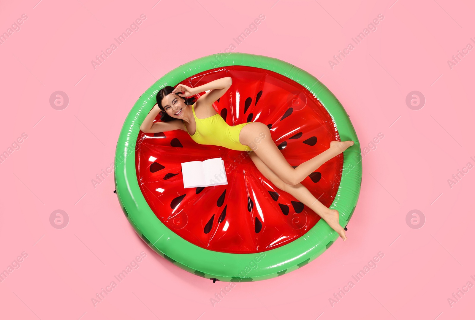 Photo of Young woman with book on inflatable mattress against pink background, above view