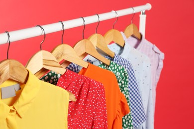 Photo of Bright clothes hanging on rack against red background. Rainbow colors
